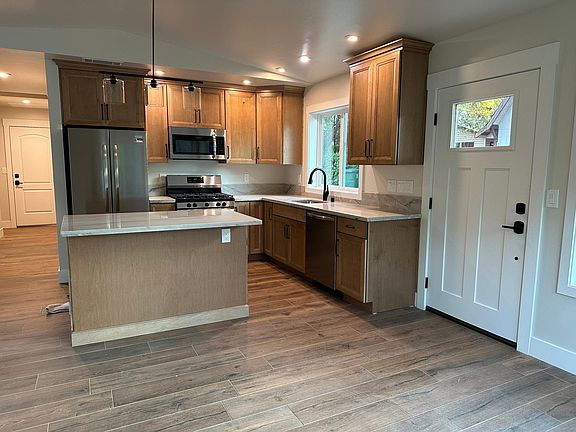 L-shaped kitchen with island: high-end cabinets, quartz countertops, stainless appliances & black accent faucet, light fixture & cabinet handles.