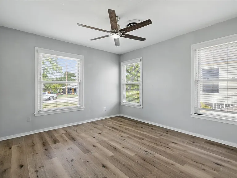 Large primary bedroom featuring neutral soft grey paint, LVP flooring, ceiling fan, closet and multiple windows providing beautiful natural light.