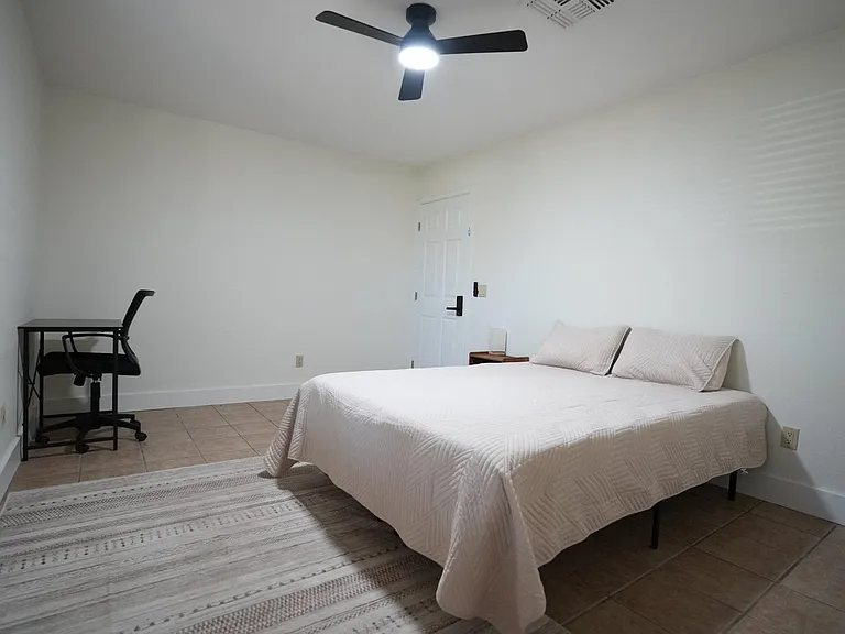 Spacious bedroom with a queen bed, ceiling fan, and tile flooring, plus a dedicated desk area for work or study.