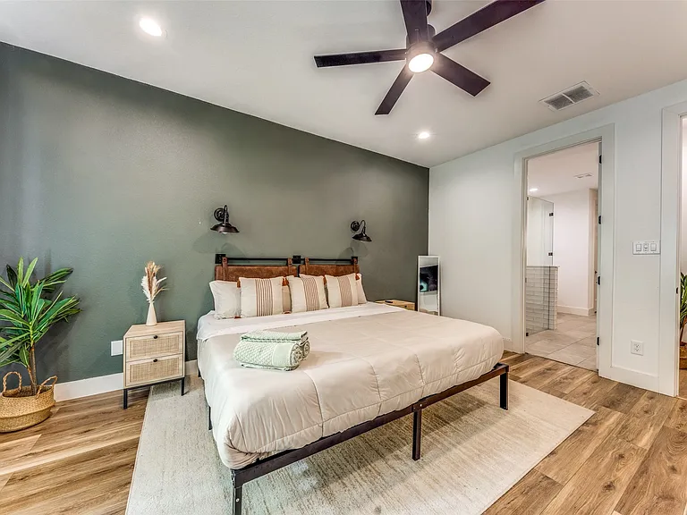 Bedroom featuring a dark accent wall, wood-finish flooring, a contemporary ceiling fan with integrated lighting, recessed lighting, and a doorway to a bathroom with tiled walls