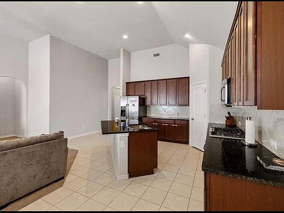Kitchen with decorative backsplash, light tile patterned flooring, dark stone countertops, stainless steel appliances, and a center island with sink