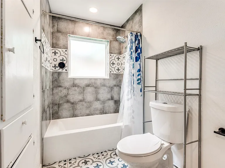 Full bathroom featuring a white tub, grey tile shower surround, and decorative accent tiles