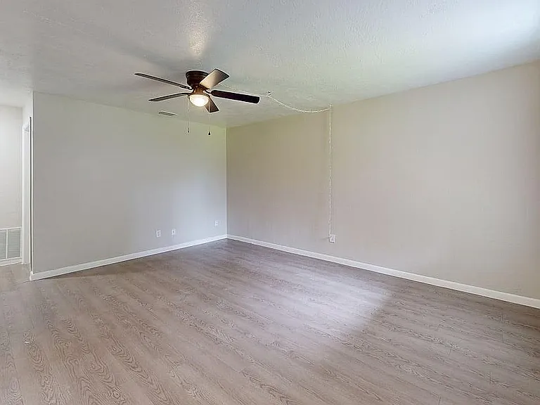 Spacious living room with modern ceiling fan, bright hardwood flooring, and ample natural light.