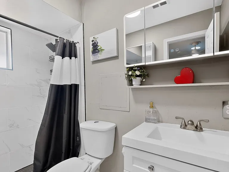 A clean primary bathroom featuring a shower, toilet, vanity and medicine cabinet, with neutral-colored tiles and bright lighting.