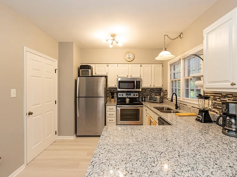 Kitchen with granite-look counters, ample white cabinetry, and stainless steel appliances plus a window over the sink.