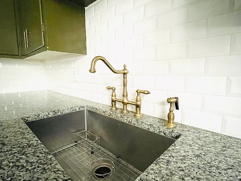 Brass bridge faucet with sprayer hose in an extra large stainless steel sink. Granite countertops throughout with custom beveled tile backsplash.