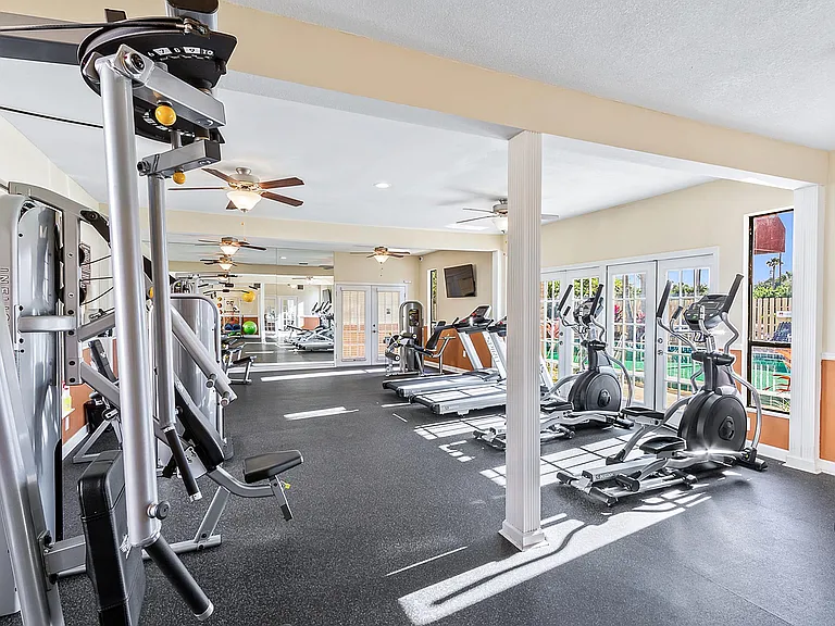 Bright and airy fitness center featuring state-of-the-art gym equipment with large windows for natural light and views of the outdoor pool.