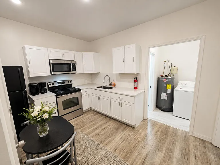 Efficient L-shaped kitchen with ample white cabinetry, full appliance set, and adjacent laundry/utility area for convenience.