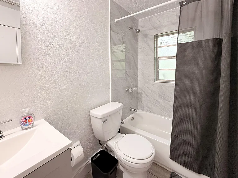 Full bath with tub/shower combo, tile surround, vanity sink, and a window for ventilation and natural light.