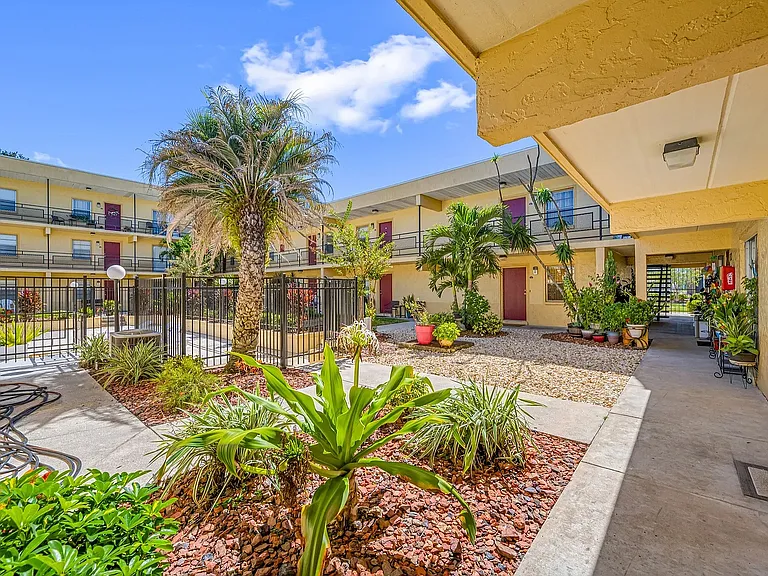 Charming apartment complex with vibrant landscaping, palm trees, and inviting walkways under a bright blue sky.