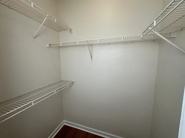 Spacious walk-in closet with sleek white shelving and natural wood-style flooring. Spacious walk-in closet with sleek white shelving and natural wood-style flooring.