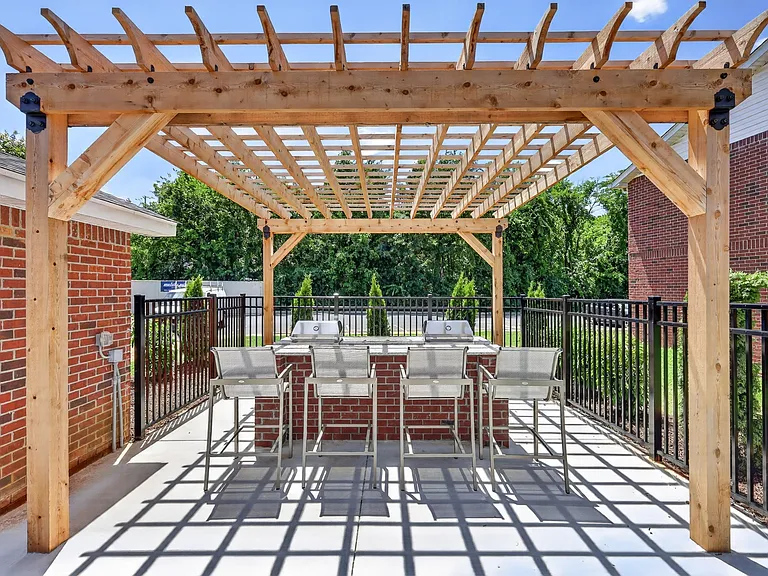 Outdoor pergola with bench seating surrounded by beautifully landscaped grounds at Saddlebrook Apartments.