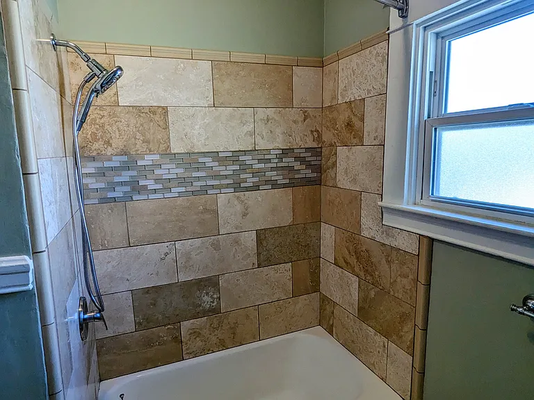 Elegant travertine floor and shower surround with mosaic tile accents.
