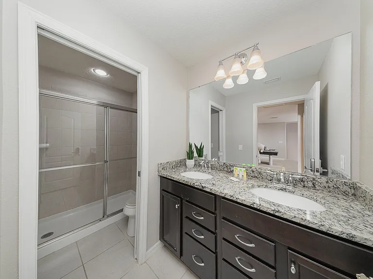 This bathroom features a dual-sink granite vanity with rich cabinetry and a glass-enclosed shower for convenience and style.