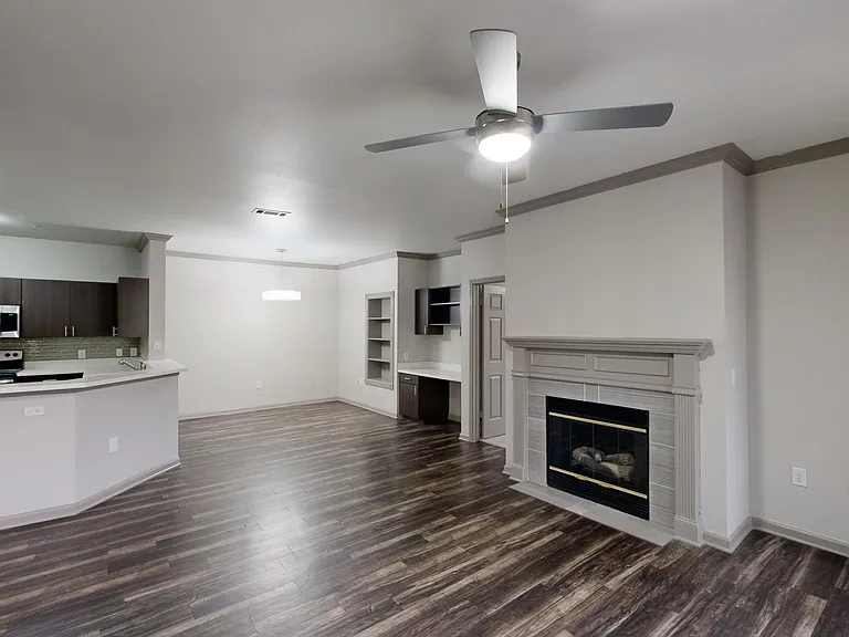 Apartment kitchen with stainless steel appliances, dining and living room with wood-style flooring and fireplace.