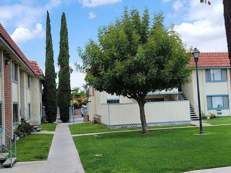 Walkway and beautiful trees and grass at Magnolia Apartments in Riverside, California.