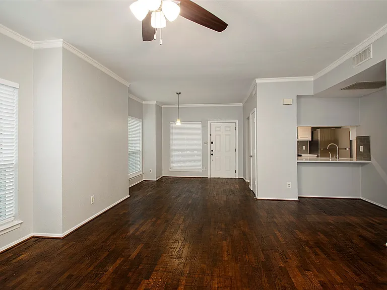 Expansive living area featuring rich wood-finish flooring, crisp white crown molding, and neutral wall tones