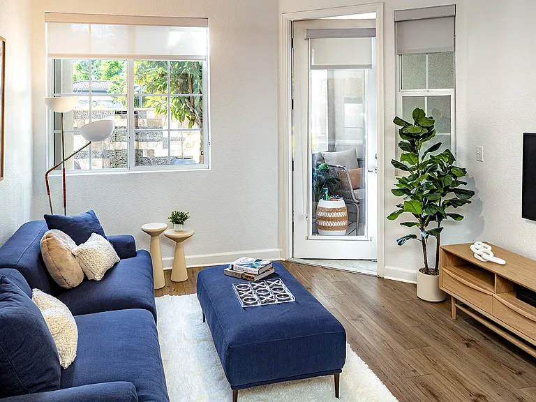 A living room with a blue sectional, a media console, and a door leading to a private patio.