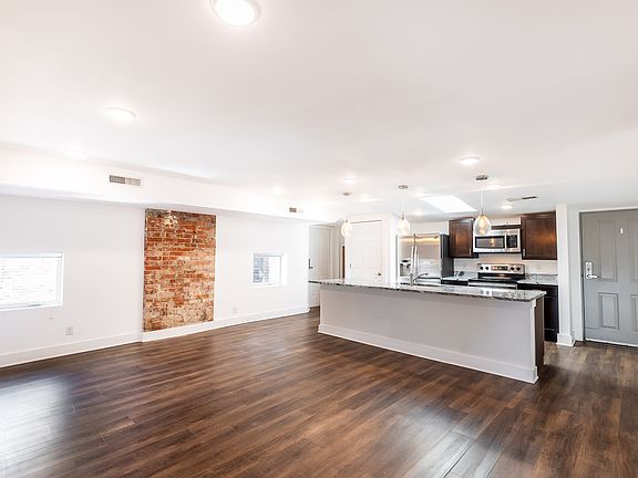 Un-staged photo shows off the luxury vinyl plank floors, large island, and exposed brick.