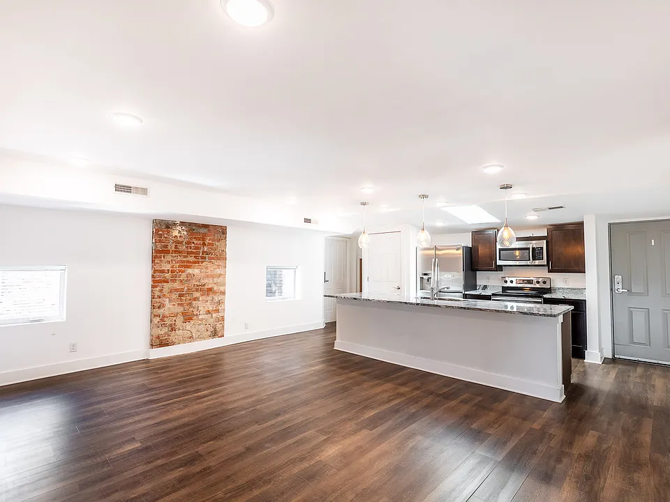 Un-staged photo shows off the luxury vinyl plank floors, large island, and exposed brick.