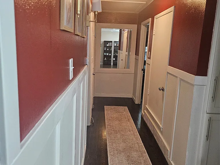 Hallway featuring dark wood-style floors, wainscoting, and a decorative wall