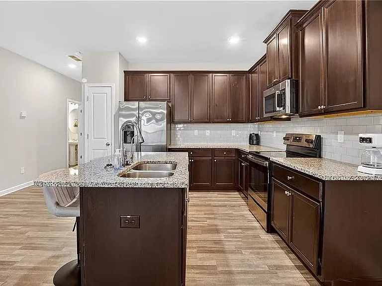 Spacious kitchen with granite island seating, stainless appliances, ample cabinetry, and subway-tile backsplash.