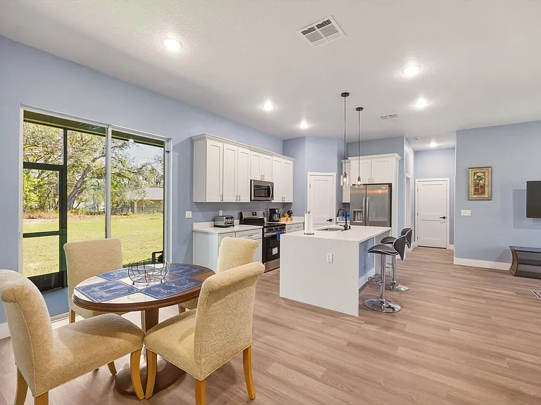 Open-concept kitchen with a large island breakfast bar, stainless appliances, and an adjacent dining nook by picture windows.