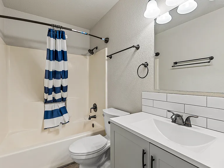Bathroom with shower/tub combo and vanity with tile backsplash.