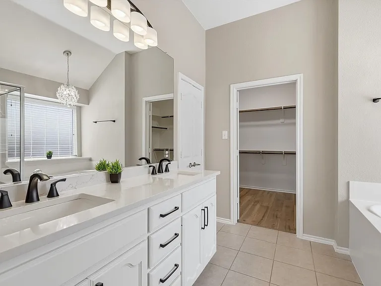 Dual vanity with quartz-finish countertop and black fixtures, featuring a large mirror and overhead lighting