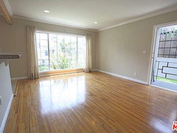 Spacious living room with picture window welcomes lots of natural light and a lush view of front yard greenery. View from hall unfurnished. Front door entrance features mid-century modern railing.