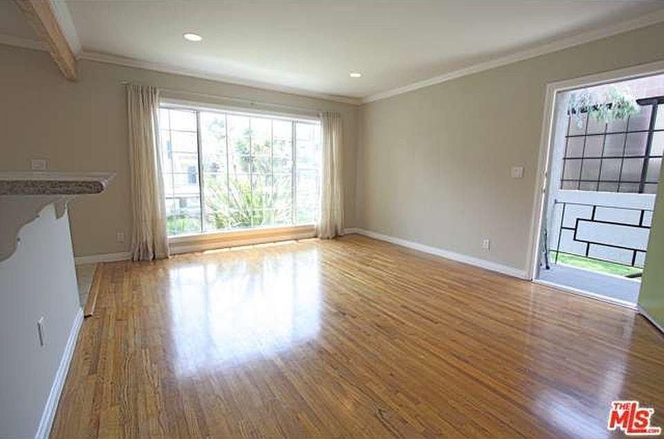 Spacious living room with picture window welcomes lots of natural light and a lush view of front yard greenery. View from hall unfurnished. Front door entrance features mid-century modern railing.