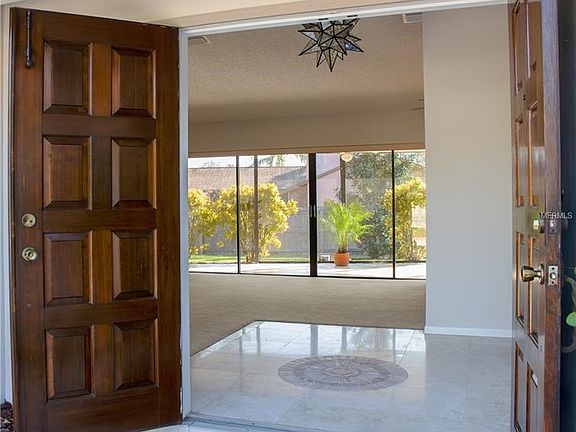 Custom carved double wooden doors open to beautiful travertine flooring in the grand foyer.