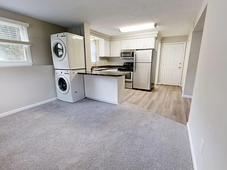 Enjoy the open-concept living space in The Valley floor plan at Alpine Commons Apartments. Featuring a modern kitchen with stainless steel appliances, in-unit washer and dryer, and cozy carpeted living area.