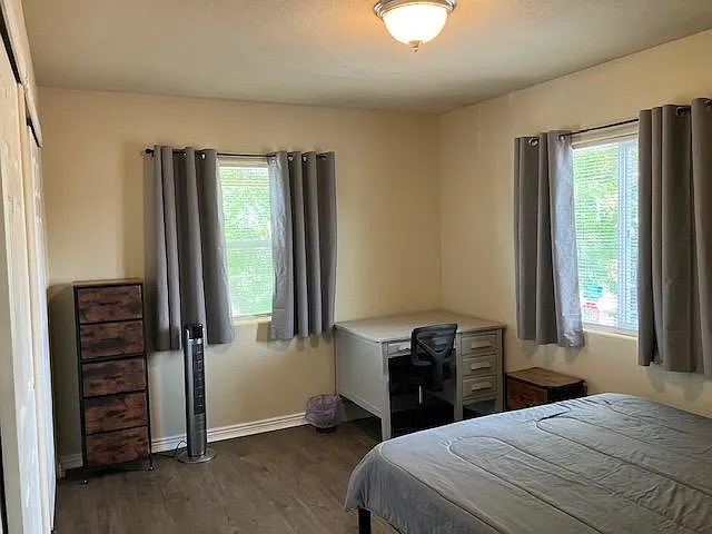 Furnished bedroom with two windows, a dedicated desk workspace, and a dresser for convenient storage.