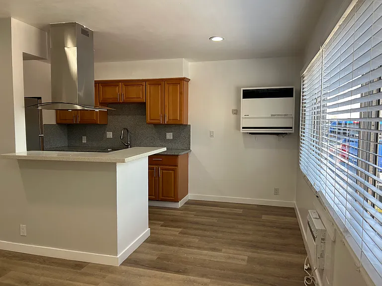 Kitchen to the left, dining area to the right, wall heater in back, natural light from window on left.