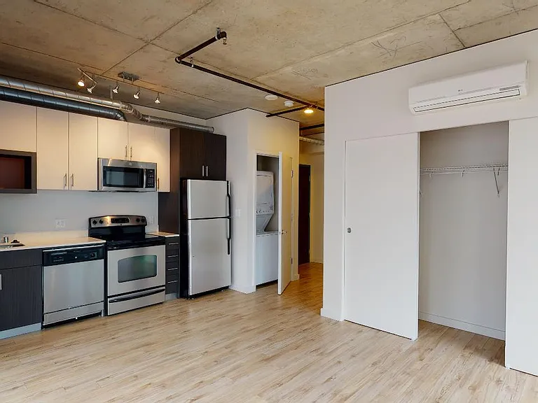 Apartment kitchen with stainless steel appliances, dining and living room with wood-style flooring.