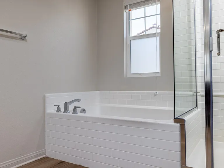 Elegant master bathroom featuring a bright soaking tub and glass-enclosed shower. Natural light fills the space, highlighting the sleek white tile and modern laminate flooring_creating a relaxing, spa-like retreat within this beautiful Menifee home.
