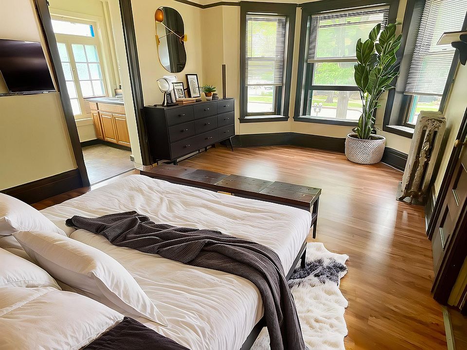Bright and inviting bedroom with elegant wooden flooring, large windows, and chic decor, creating a serene and stylish sanctuary.