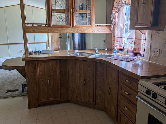 Looking through kitchen to living room. Corner sink with overhead glass cabinetry. Large windows on both sides of living room provide natural light throughout the day. Breakfast bar can be seen on left.