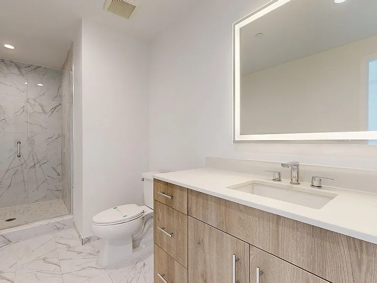 Apartment Bathroom with glass enclosed shower, LED vanity mirror and tile floors.