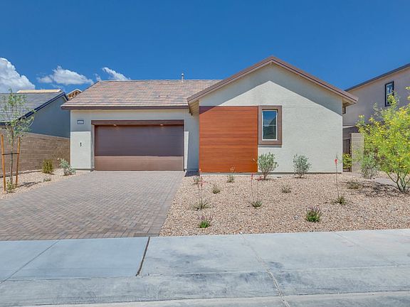 A modern, single-story house with a garage, surrounded by a paved driveway and landscaped with deser