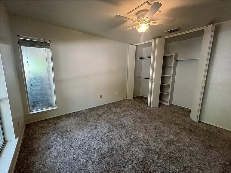 Spacious room featuring neutral carpeting, a ceiling fan with integrated lighting, and two built-in closet spaces with shelving and hanging rods