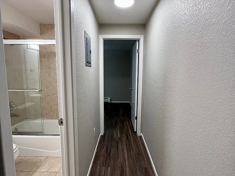 Elegant apartment hallway with modern wood flooring and a brightly lit bathroom entrance.