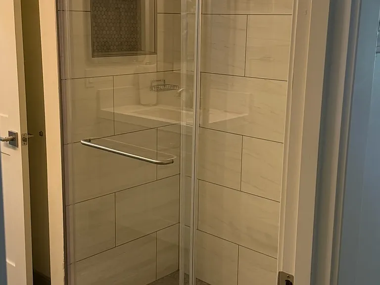 Downstairs hall bathroom has large glass door enclosure and tiled shampoo niche