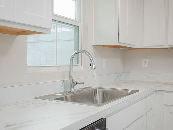 The kitchen includes a deep and wide stainless steel sink under a window overlooking the backyard, with conveniently placed dishwasher