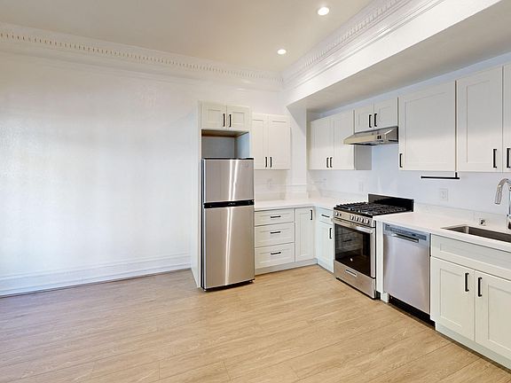 Kitchen with multiple cabinets, refrigerator, stove, range hood, and sink