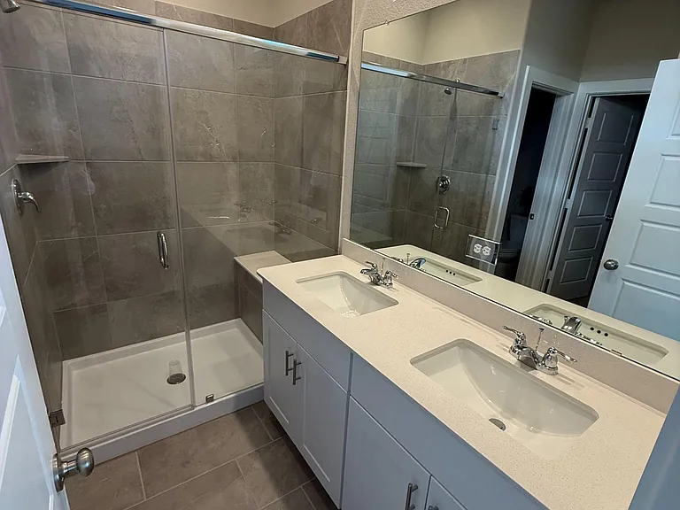 Spacious bathroom with a double-sink vanity, large wall mirror, and a tiled shower/tub combo for easy daily routines.
