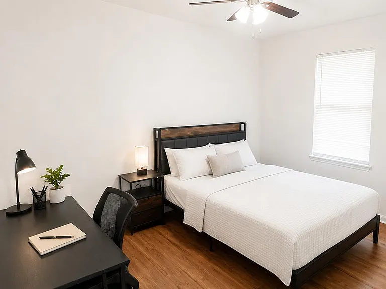 Furnished bedroom with a full bed, nightstand, and dedicated desk/workspace, plus wood-look flooring and ceiling fan.