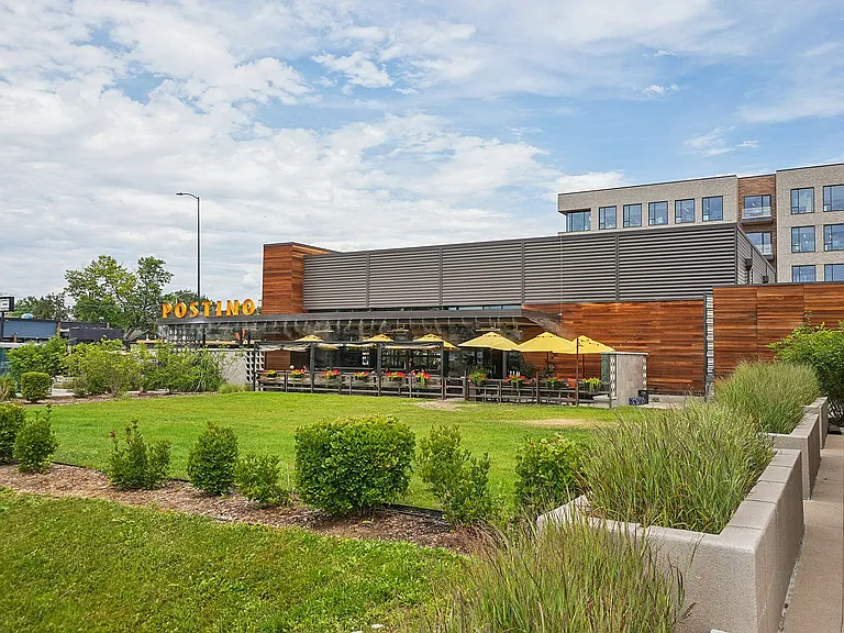 Charming outdoor view of a modern restaurant with wooden accents, vibrant yellow umbrellas, and lush green landscaping.