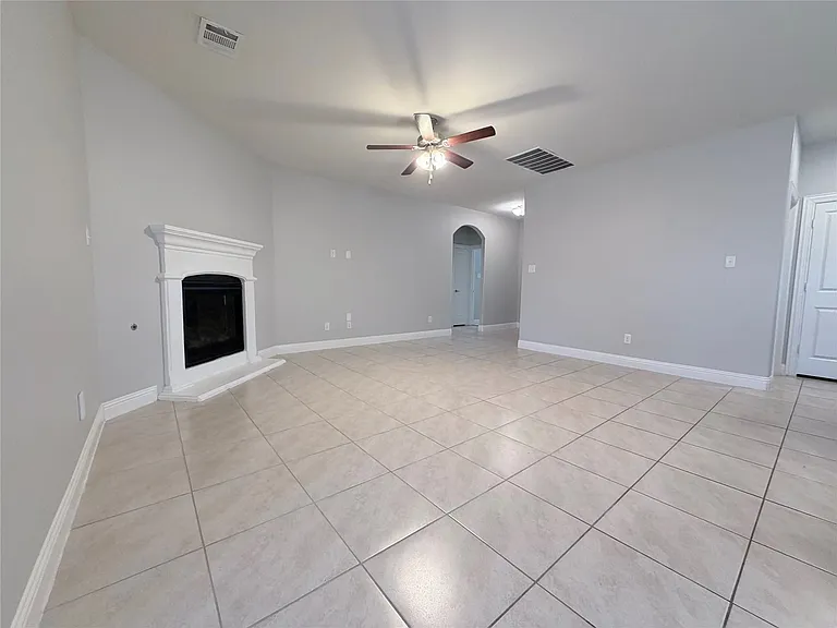 This spacious and inviting living area is designed for comfort and style, featuring durable and elegant tile flooring that spans the entire room. The space is well-lit and climate-controlled with a modern ceiling fan that includes an integrated light fixt